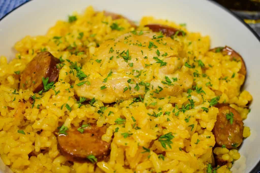 Yellow Spanish Rice with chicken and sausage served in a white bowl.