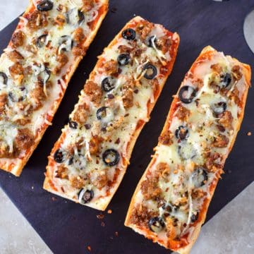 An image of three pieces of the French bread pizza arranged on a black cutting board.