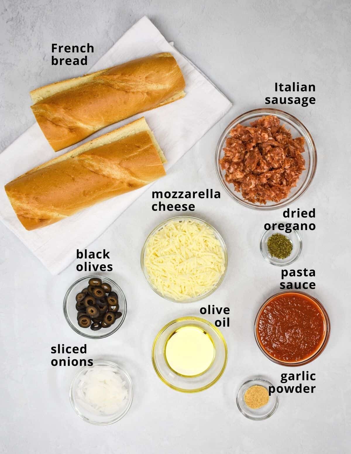 The ingredients for the pizza arranged on a white table and labeled in small black letters.