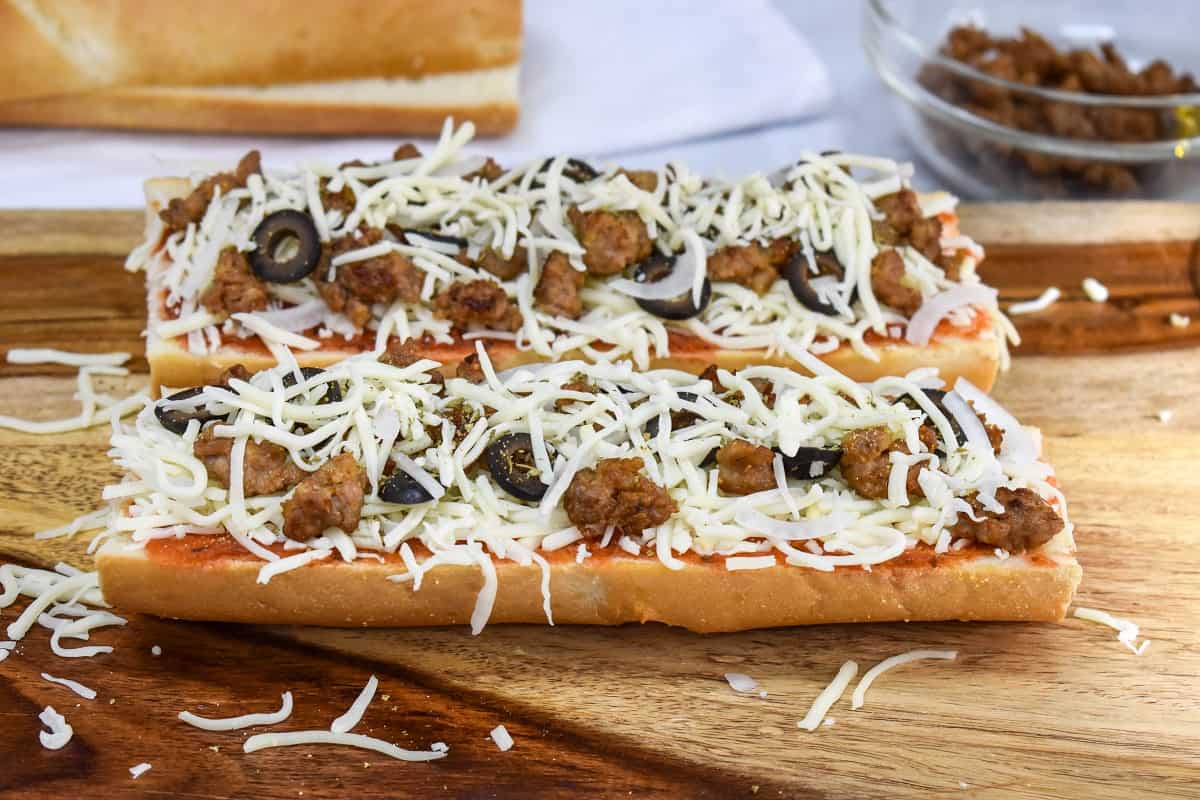 An image of the French bread pizza before baking, on a wood cutting board.