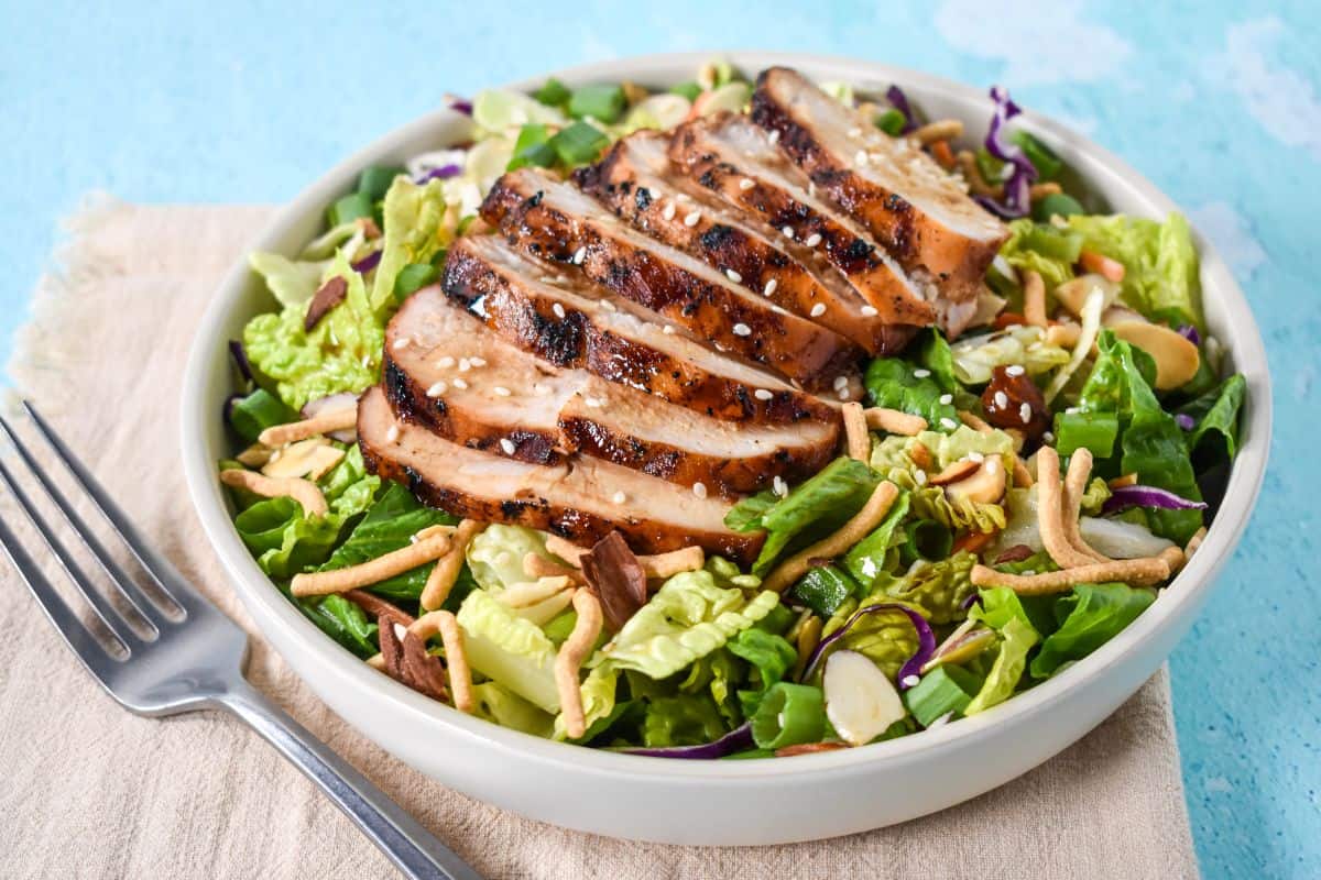 Close-up of sesame chicken chopped salad with grilled chicken slices, greens, almonds, and noodles.