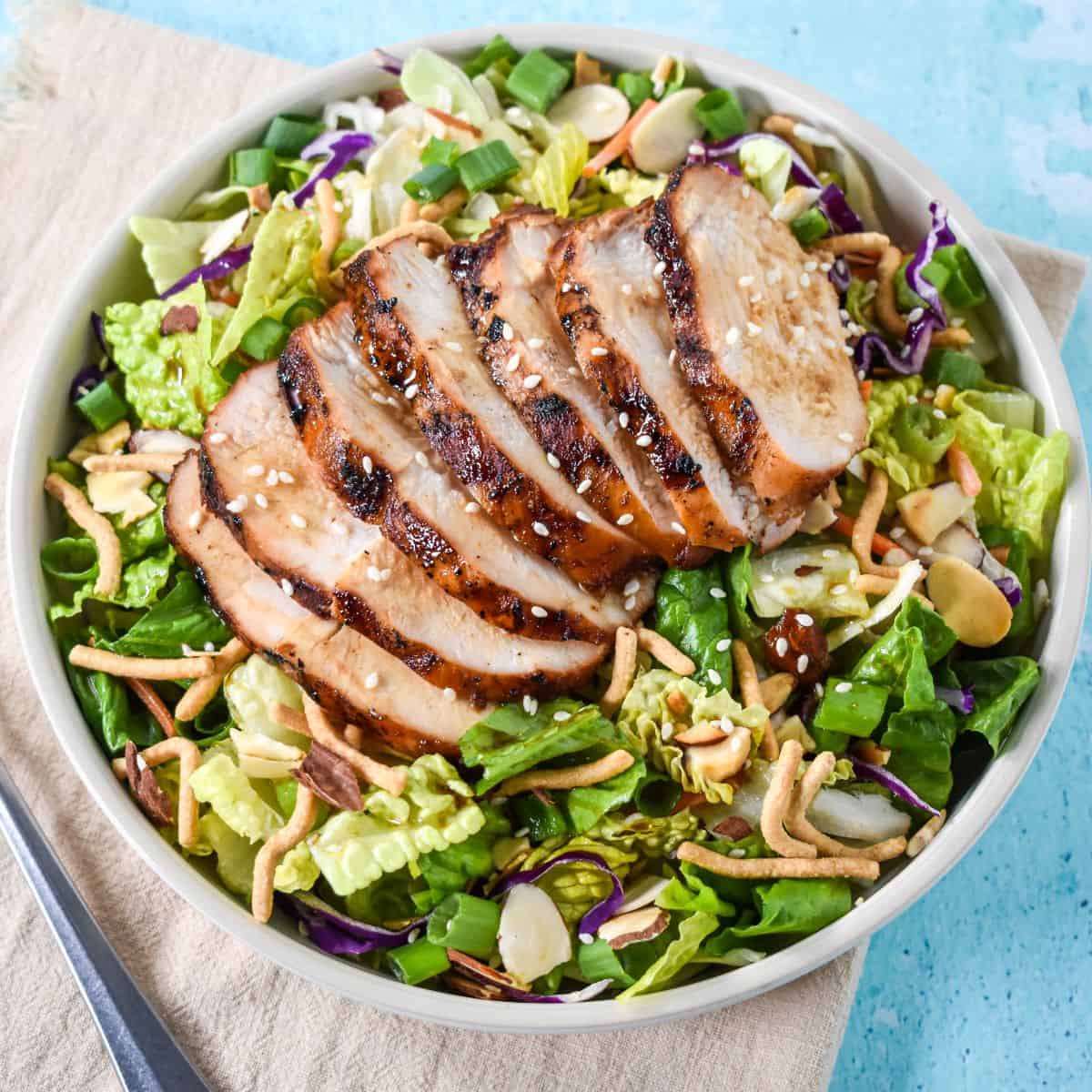 Bowl of sesame chicken chopped salad with grilled chicken, cabbage, lettuce, and crunchy toppings.