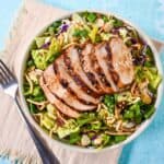 Bowl of sesame chicken chopped salad with grilled chicken, cabbage, lettuce, and crunchy toppings.