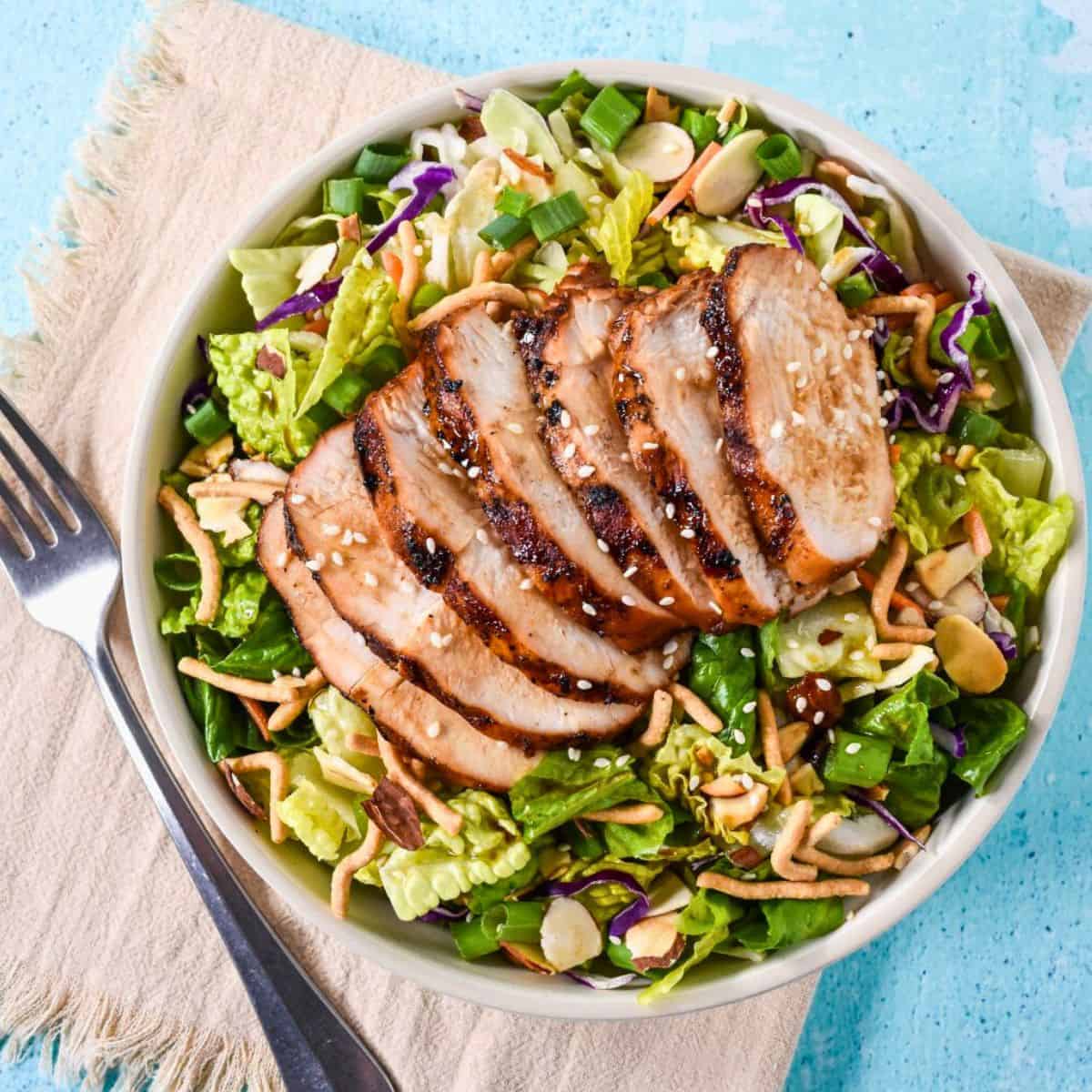 Bowl of sesame chicken chopped salad with grilled chicken, cabbage, lettuce, and crunchy toppings.