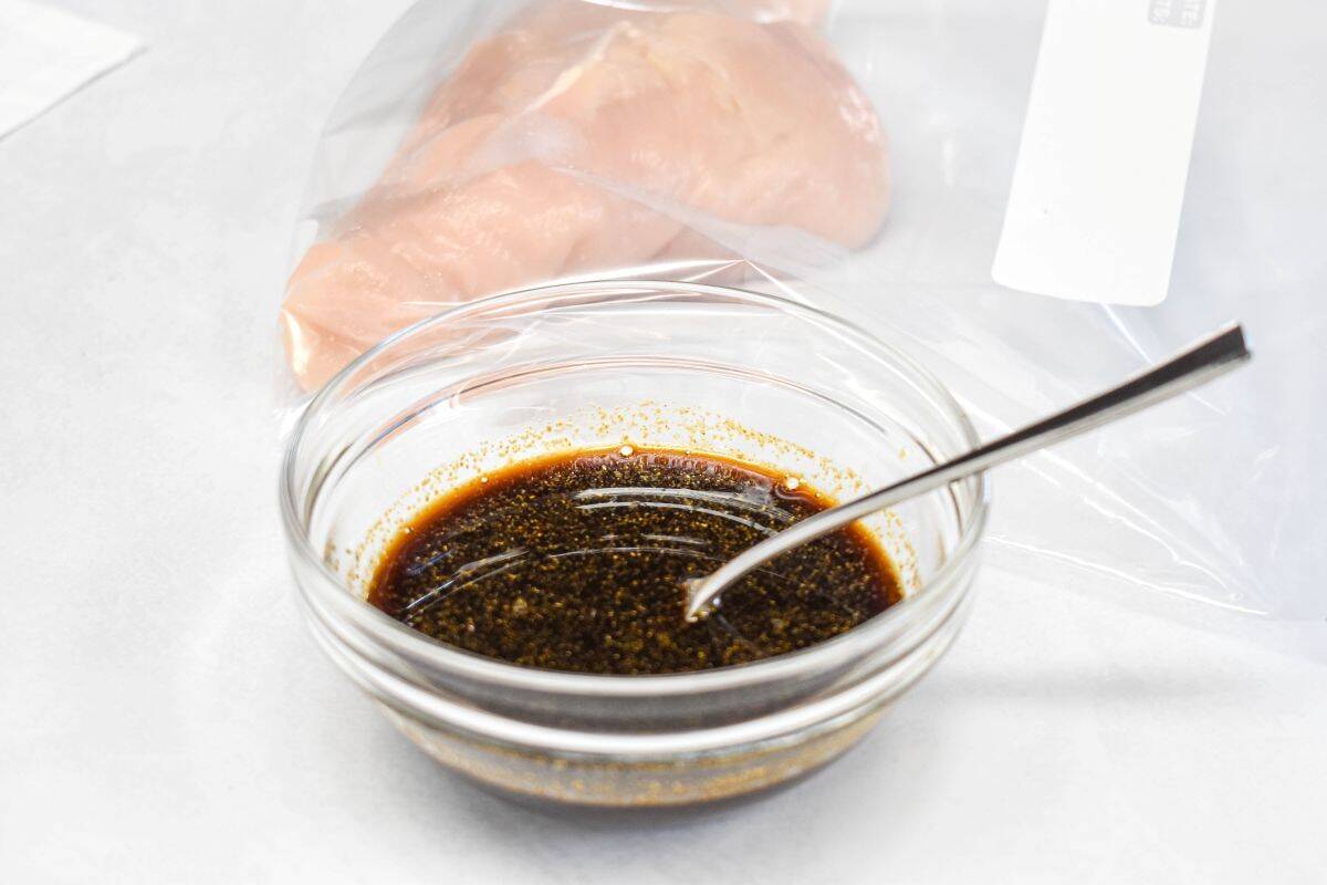 Chicken marinade in a glass bowl with raw chicken in a plastic bag in the background.