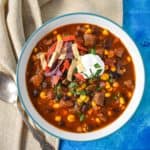 The southwestern steak soup served in a white bowl with a light blue rim set with a beige linen on a blue table.