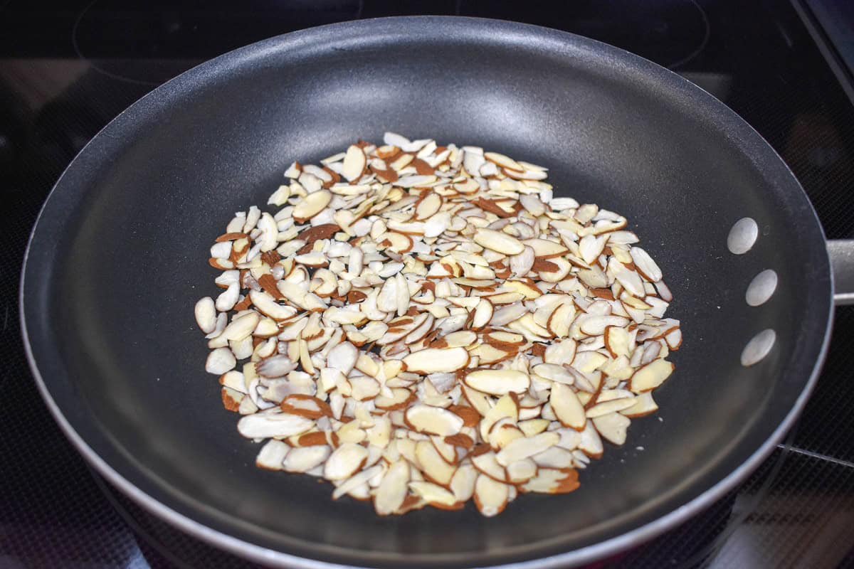 Sliced almonds being toasted in a non-stick skillet on the stove.