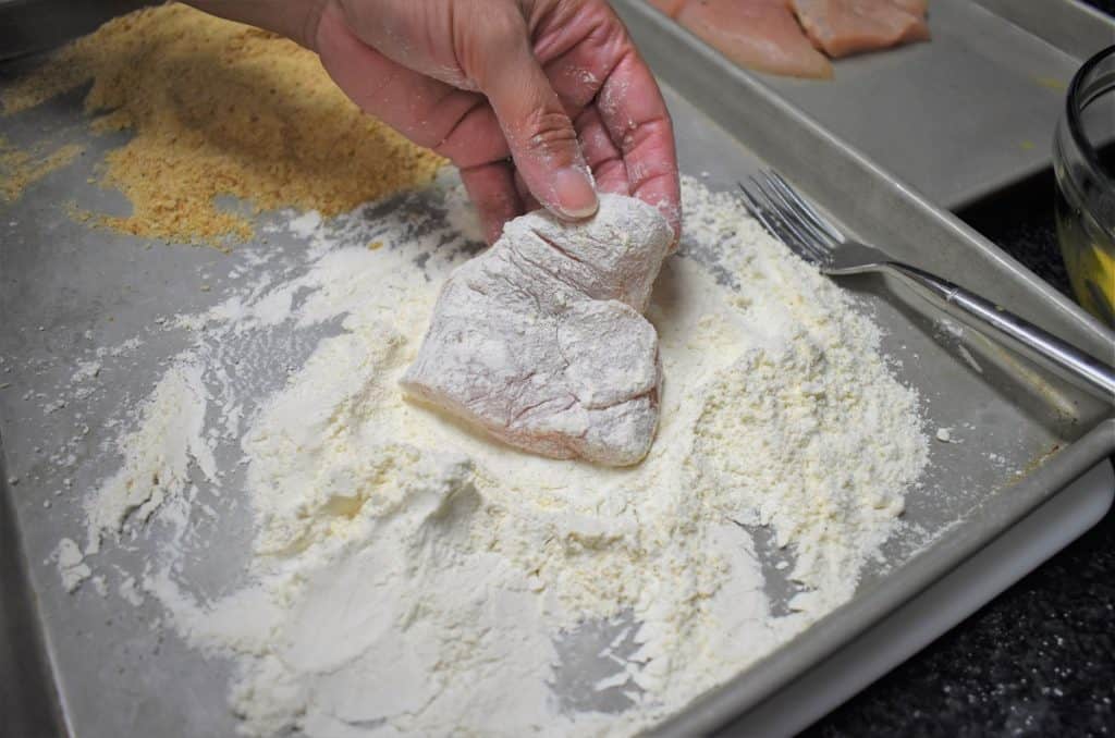 Dredging, a chicken breast cutlet being dredged in flour.