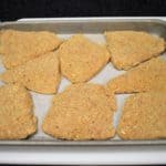 Breaded Chicken cutlets arranged on a metal pan that's lined with parchment paper