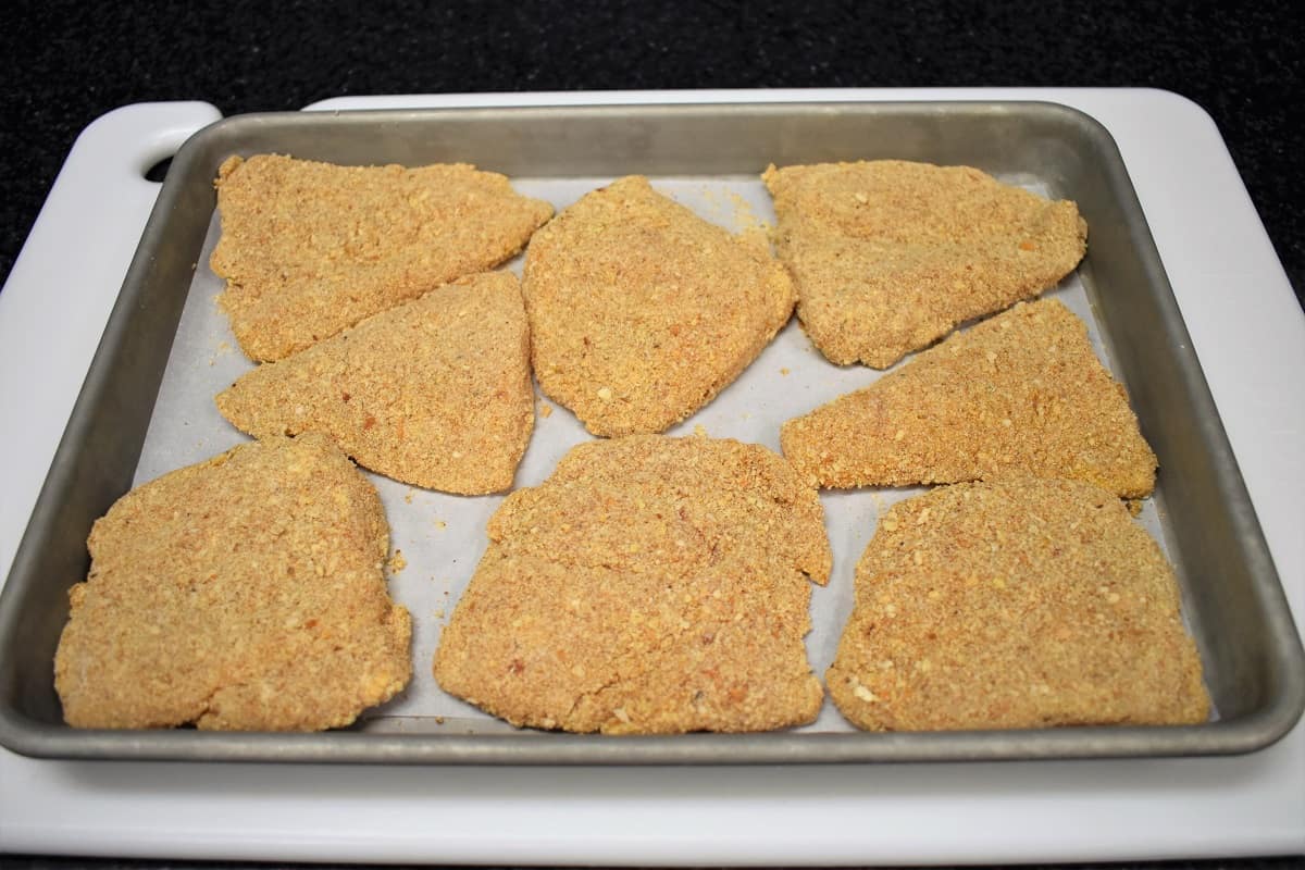 Breaded Chicken cutlets arranged on a metal pan that's lined with parchment paper