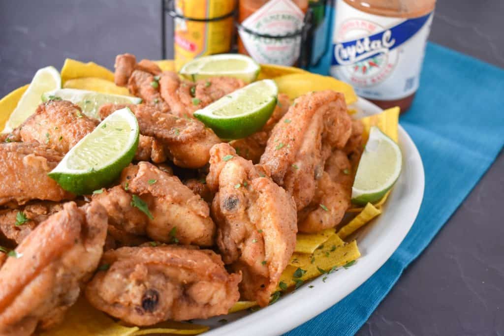 Chicharrones de pollo on a bed of plantain chips garnished with lime wedges.