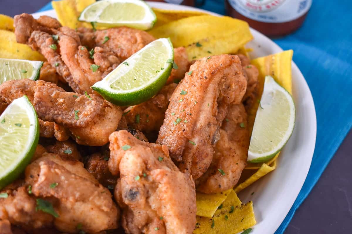 Chicharrones de pollo on a bed of plantain chips and garnished with lime wedges and chopped cilantro.