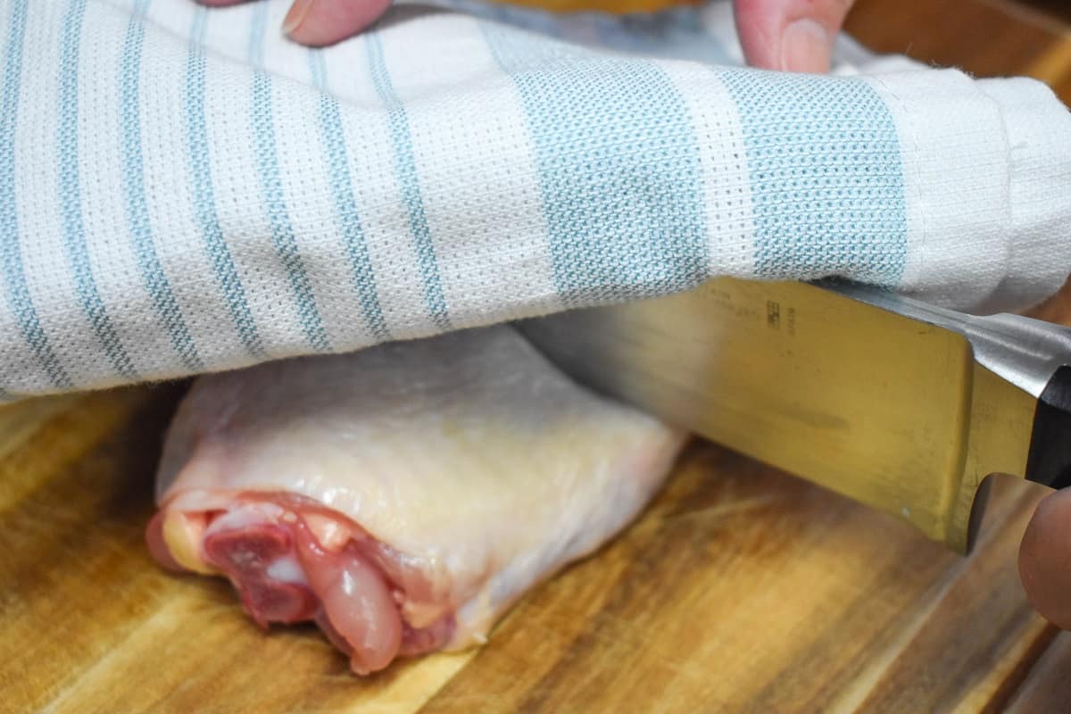 A light blue and white kitchen towel over a knife and chicken thigh.