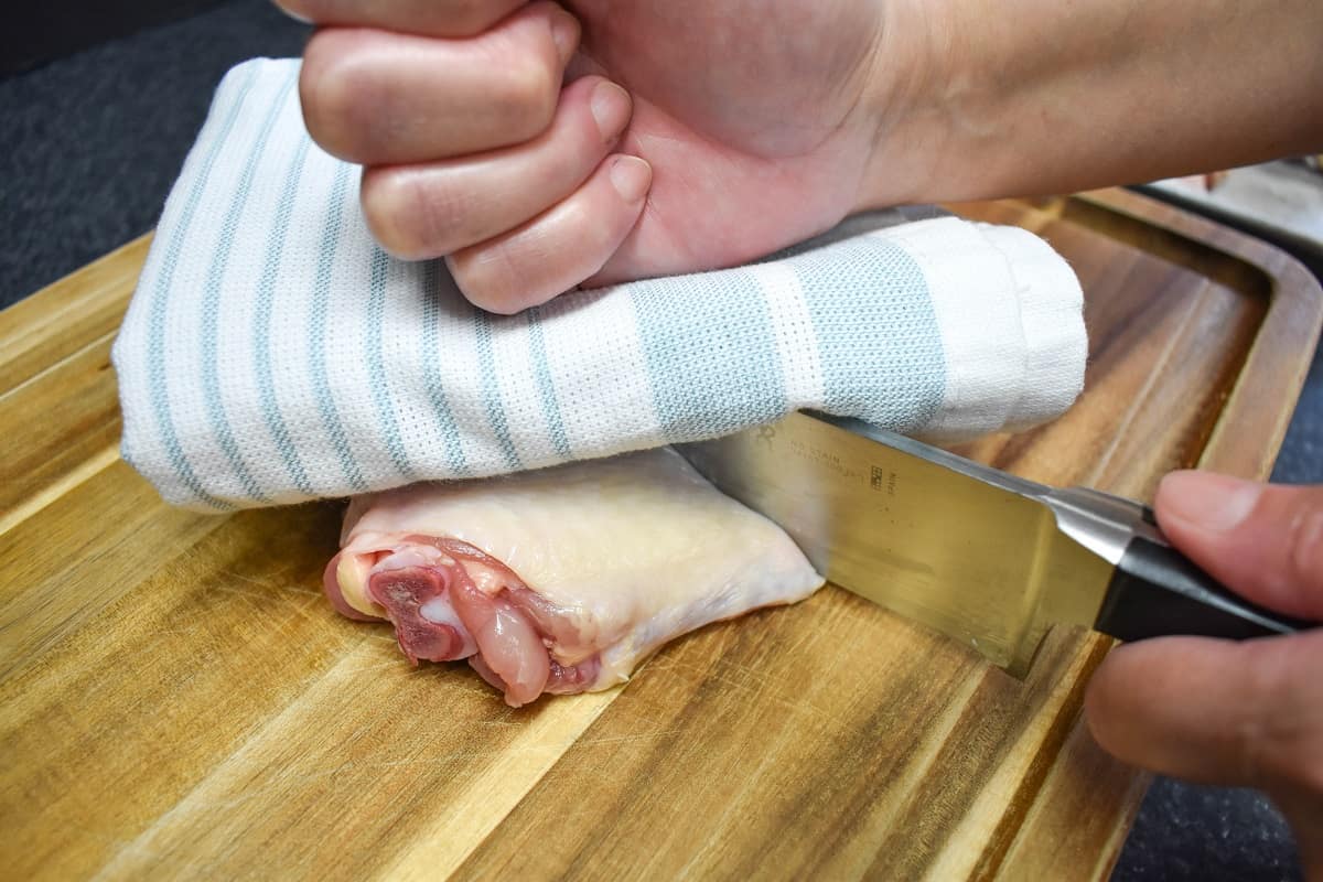 Cutting a chicken thigh by tapping a large knife covered with a kitchen towel.