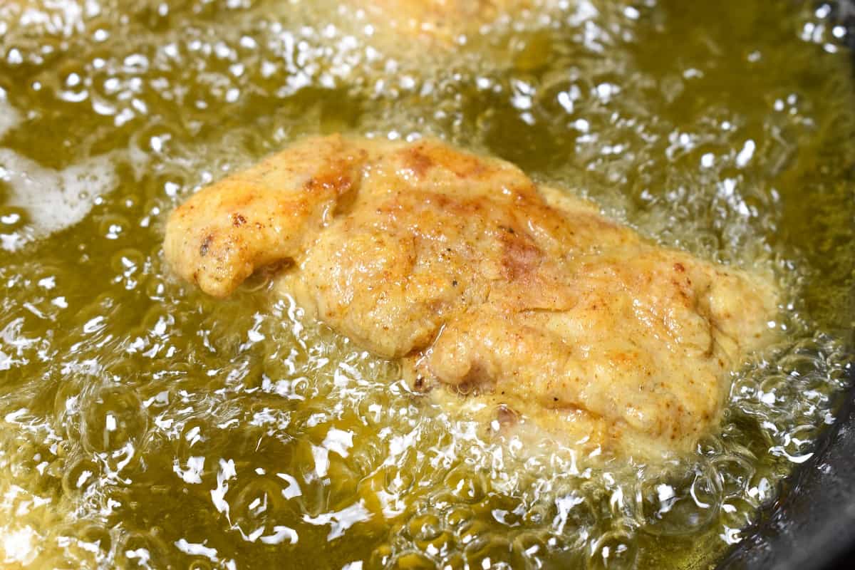 A piece of chicken frying in a skillet.