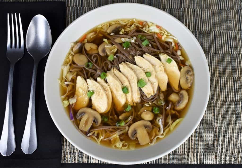 Soba Noodle Chicken Soup with mushrooms, green onions and sesame seeds served in a large, shallow light colored bowl