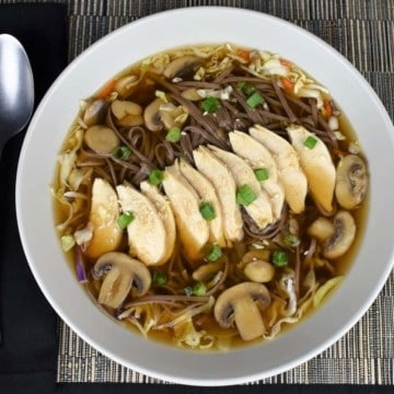 Soba Noodle Chicken Soup with mushrooms, green onions and sesame seeds served in a large, shallow light colored bowl