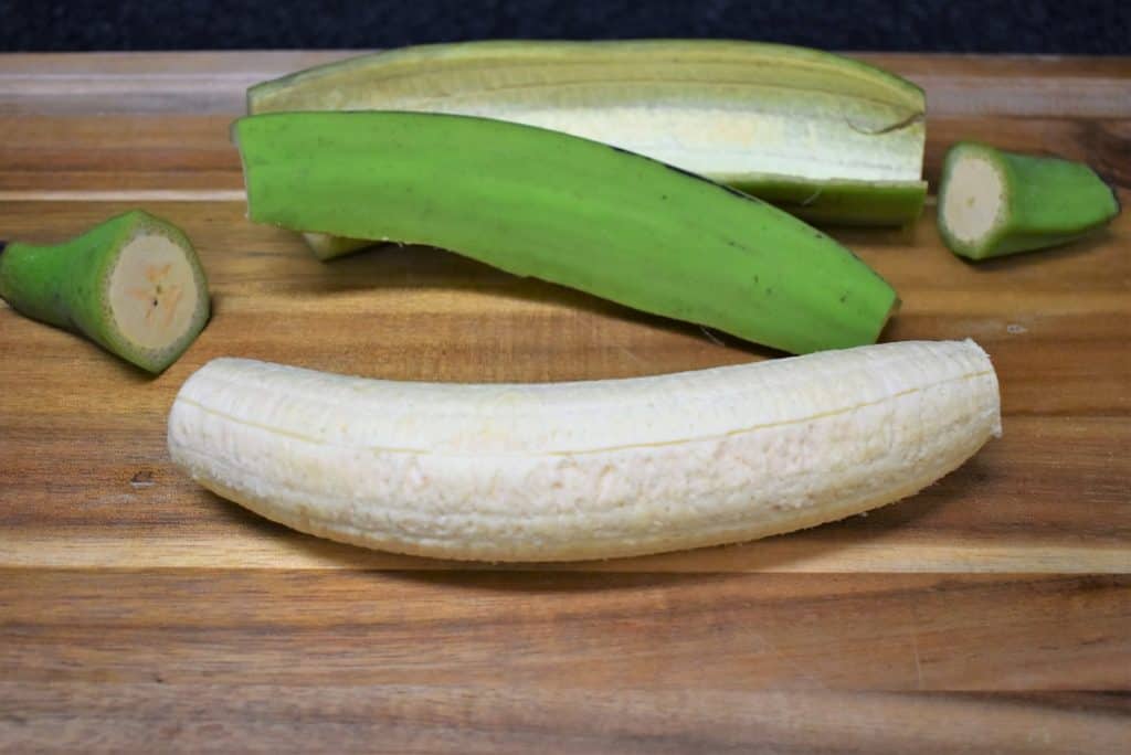 Green plantains for tostones peeled with the peel arranged behind it.