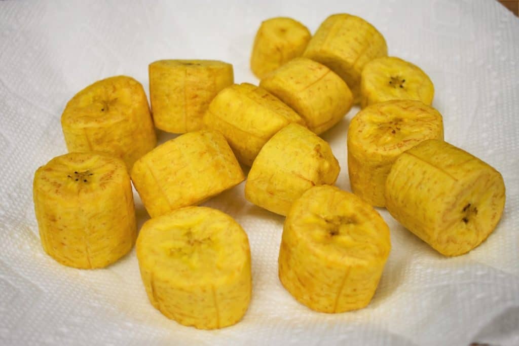 Fried green plantains without flattening for tostones arranged on a paper towel lined plate.