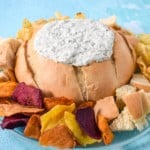An image of the creamy spinach dip served in a bread bowl with pieces of bread and chips around it.