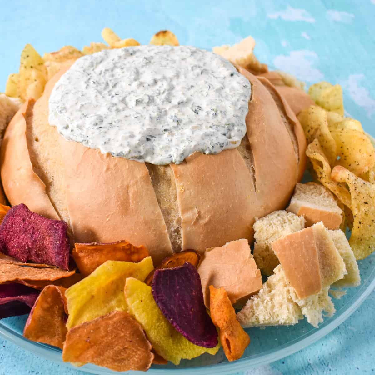 An image of the creamy spinach dip served in a bread bowl with pieces of bread and chips around it.