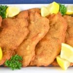 Pork Schnitzel arranged on a white platter and garnished with fresh parsley and lemon wedges.