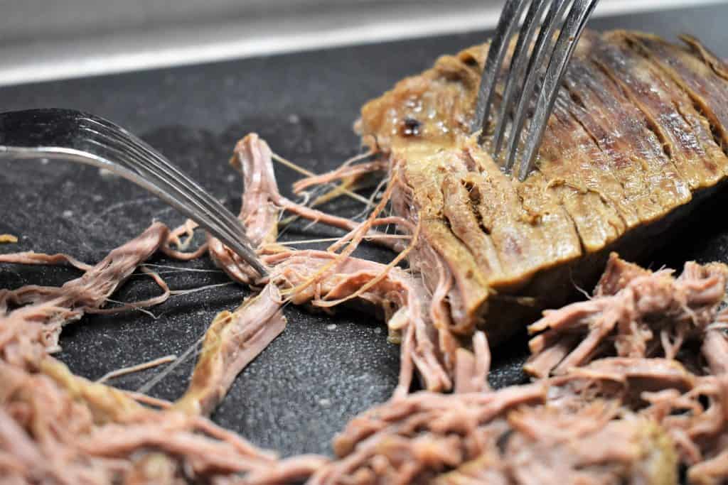 Shredding flank steak using two forks on a black cutting board.