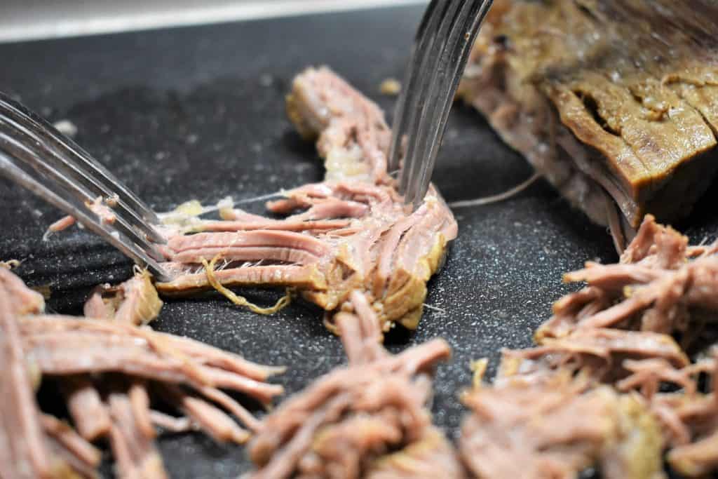 Shredding flank steak using two forks on a black cutting board.