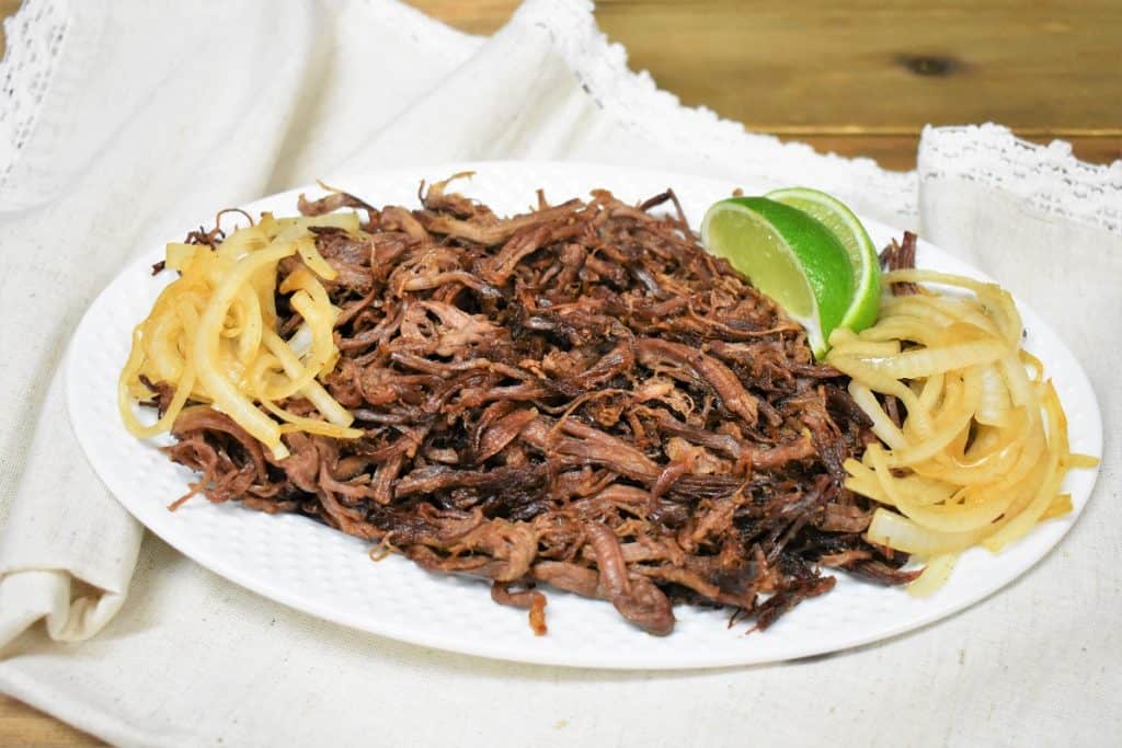 Vaca Frita served on a white platter and garnished with cooked onions and lime wedges on the side.
