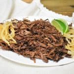 Vaca Frita served on a white platter and garnished with cooked onions and lime wedges on the side.