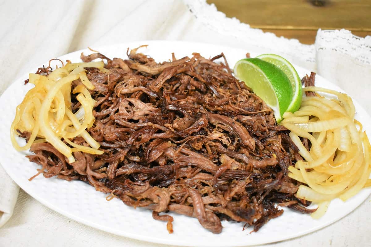 Vaca Frita served on a white platter and garnished with cooked onions and lime wedges on the side.