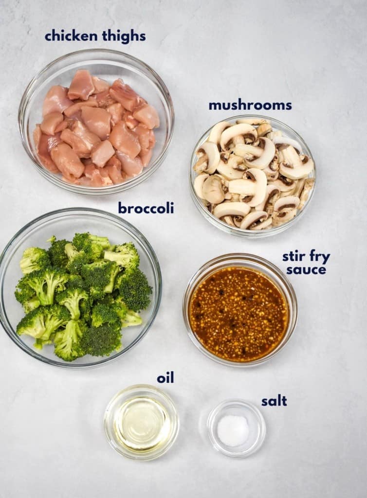 The ingredients for the dish, prepped and arranged on a white table. The sauce is prepared already and each ingredient has a label above or to the side in dark letters.
