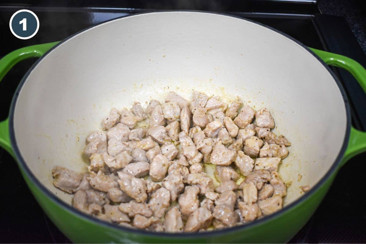 Cubed pork browning in a large green pot.