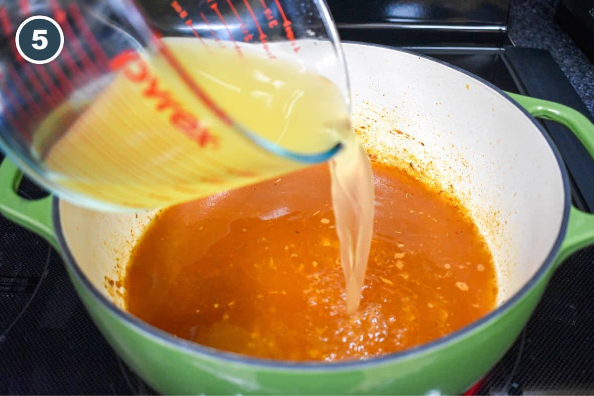 Chicken broth being poured into the pot over the sofrito mixture.
