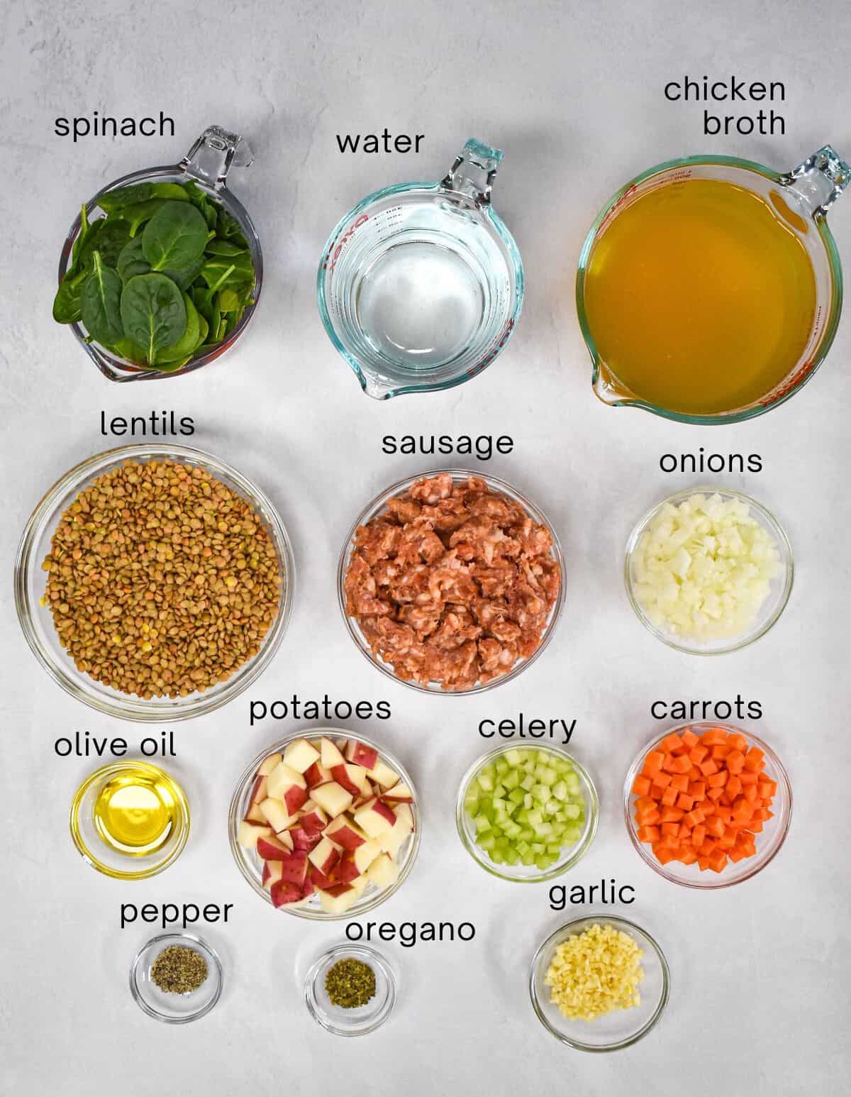 The ingredients for the lentil soup arranged in glass bowls on a white table with each one labeled with small black letters.