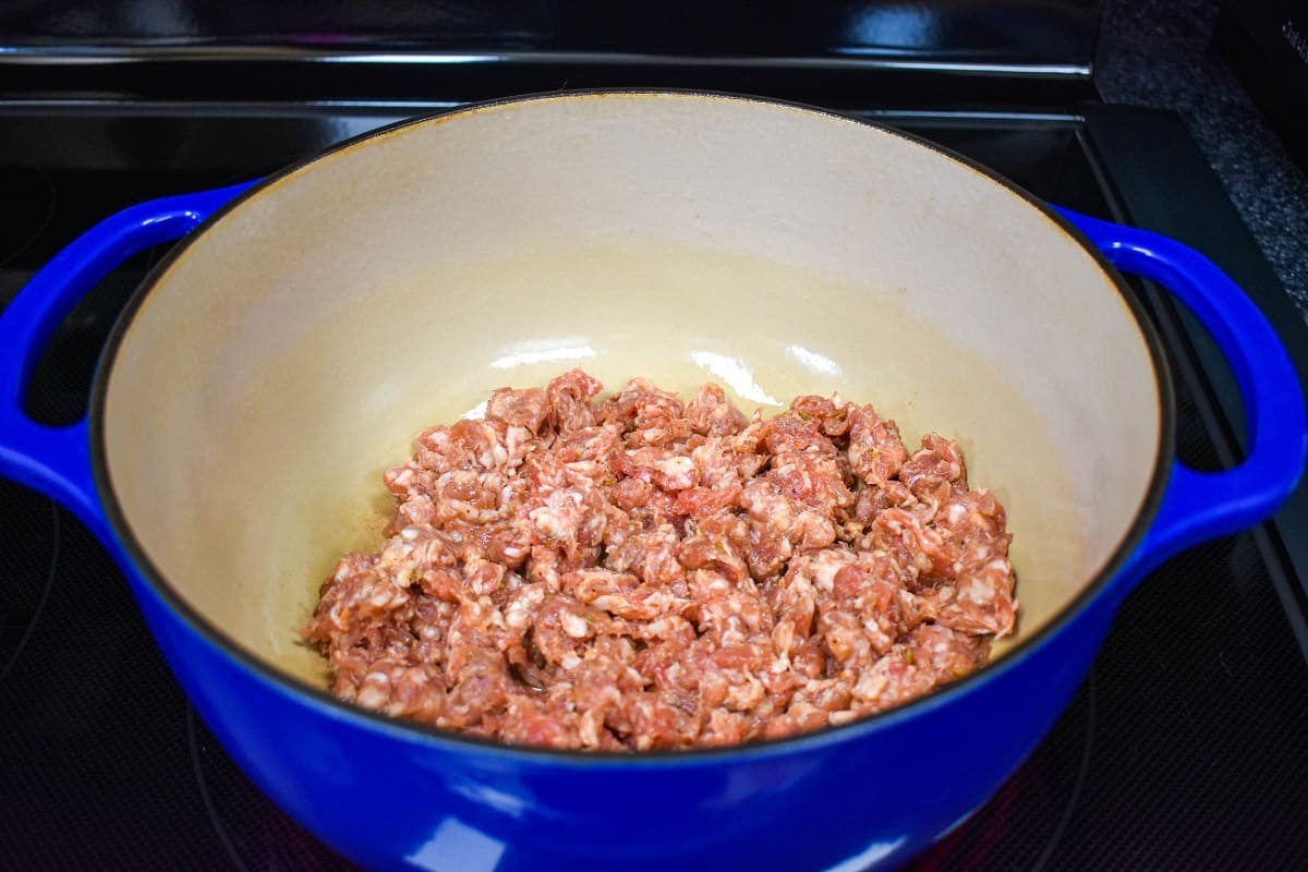 Crumbled Italian sausage added to a large, blue and white pot.
