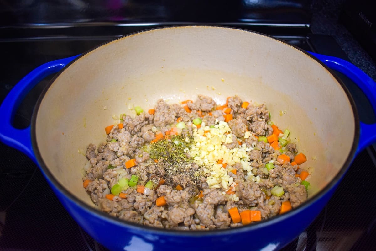 Browned sausage with onions, carrots, celery, and garlic cooking in a large, blue and white pot.