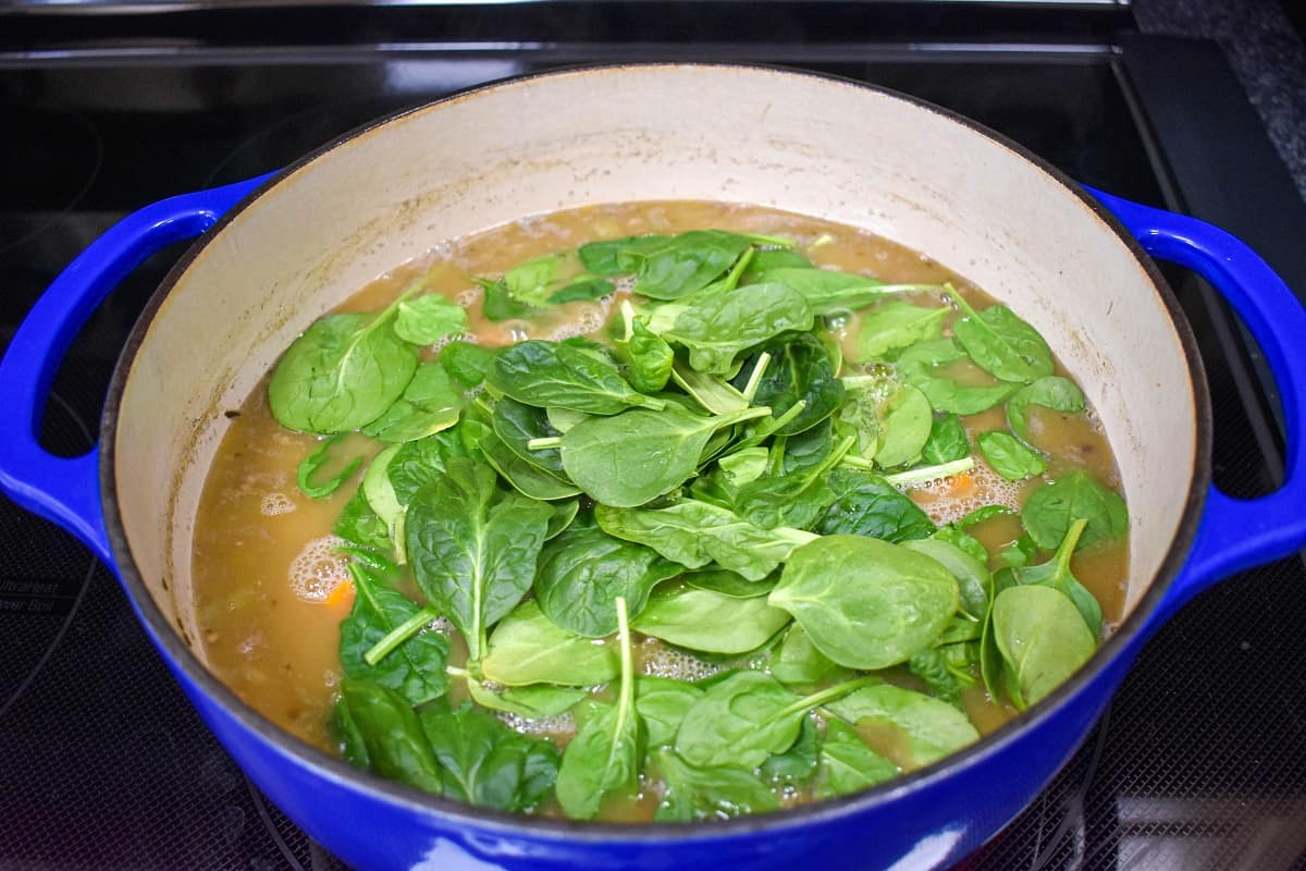 Fresh spinach added to the ingredients in a large blue and white pot.