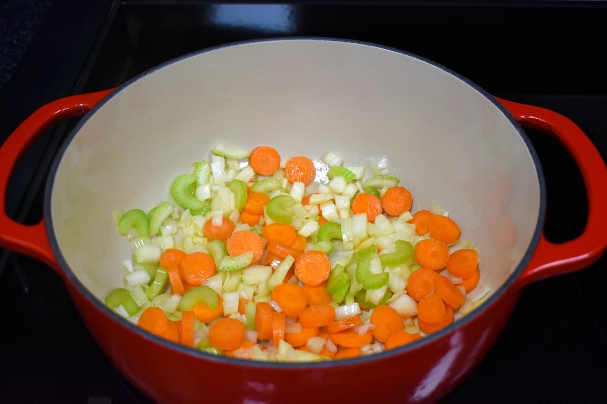 Diced onions, carrots, and celery sautéing in a large, red and white pot.