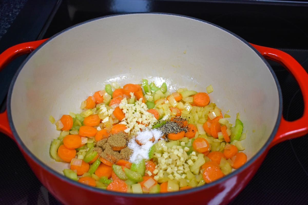 Diced onions, carrots, celery, garlic, and spices sautéing in a large, red and white pot.