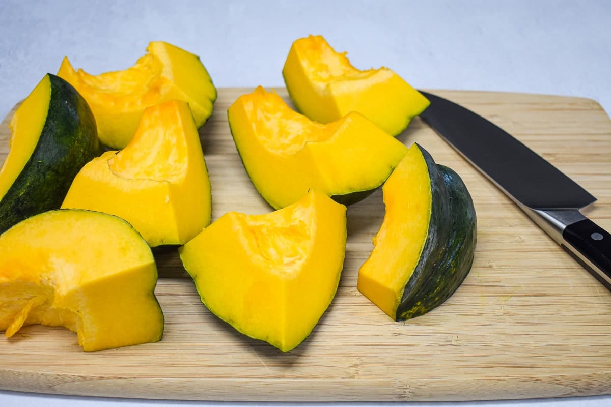 Pumpkin pieces set on a wood cutting board with a large knife to the right side.