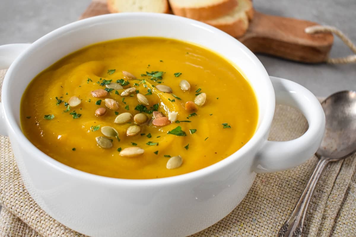 The finished soup garnished with pumpkin seeds and chopped parsley and served in a white bowl.