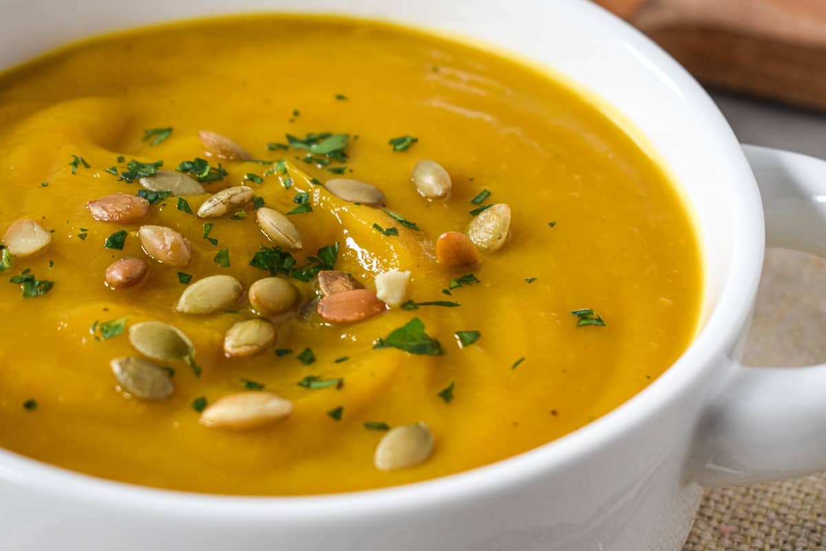 A close up of the finished soup garnished with pumpkin seeds and chopped parsley and served in a white bowl.