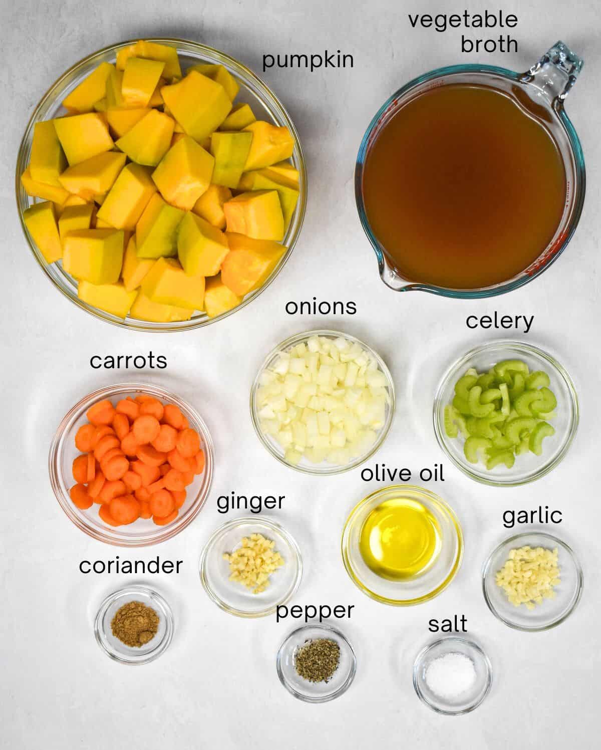 The ingredients for the soup arranged in glass bowls on a white table with each labeled in small black letters.