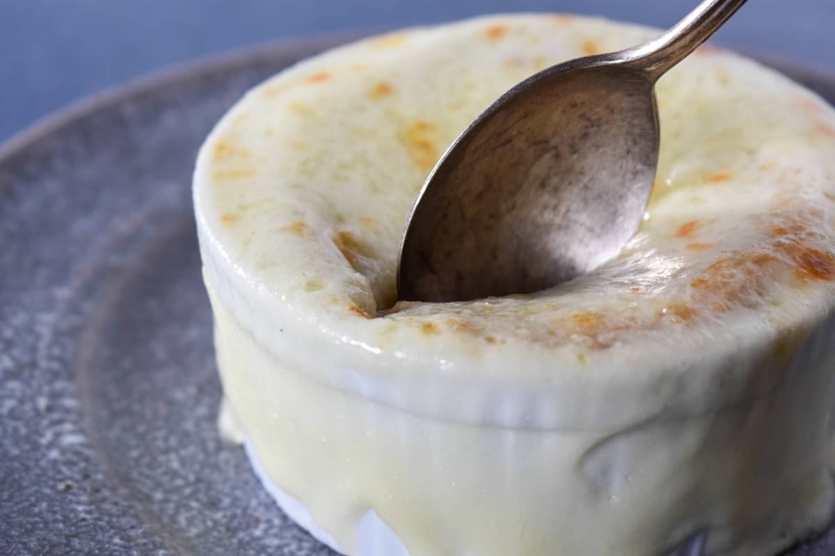 A spoon going into the cheese topping on french onion soup served in a small white bowl.