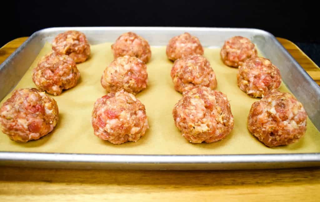 Twelve raw meatballs arranged on a baking sheet lined with parchment paper.