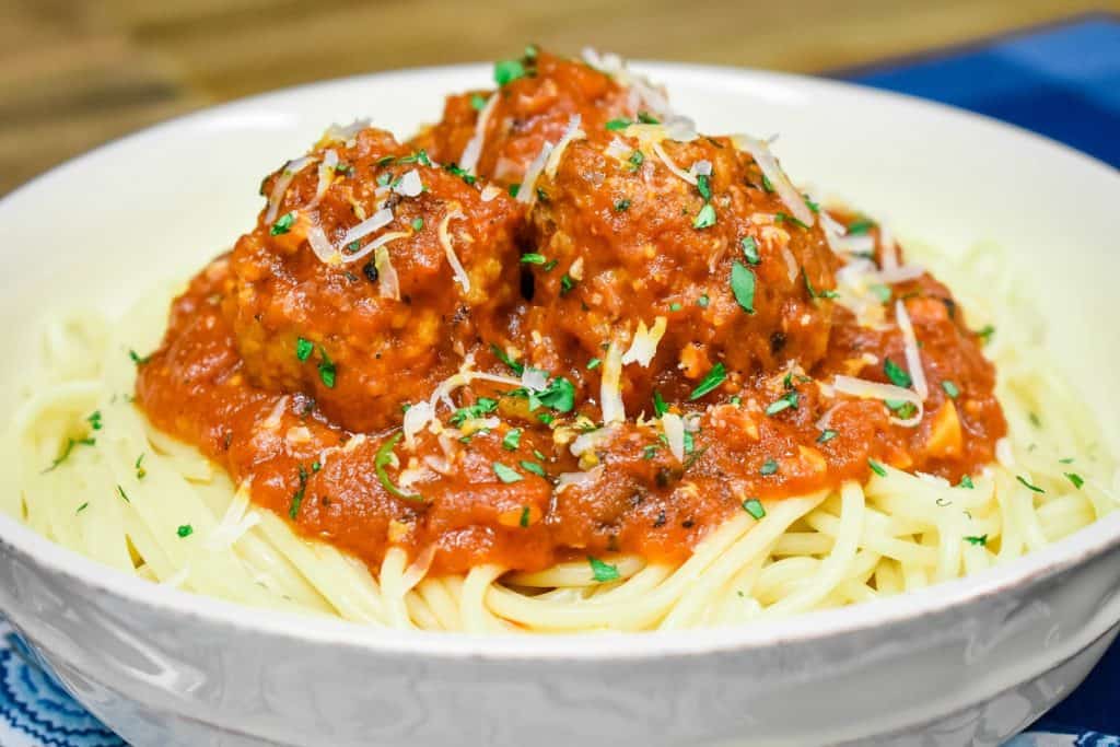 Italian sausage meatballs in a red sauce, served on a bed of spaghetti in a white bowl and garnished with chopped parsley and grated Parmesan cheese.