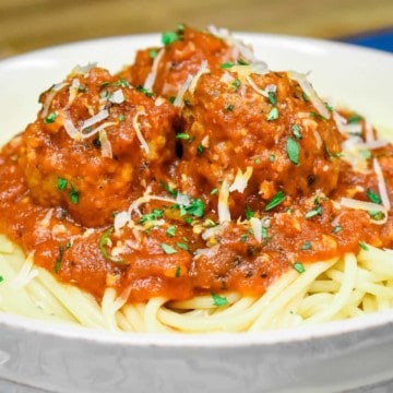 Italian sausage meatballs in a red sauce, served on a bed of spaghetti in a white bowl and garnished with chopped parsley and grated Parmesan cheese.