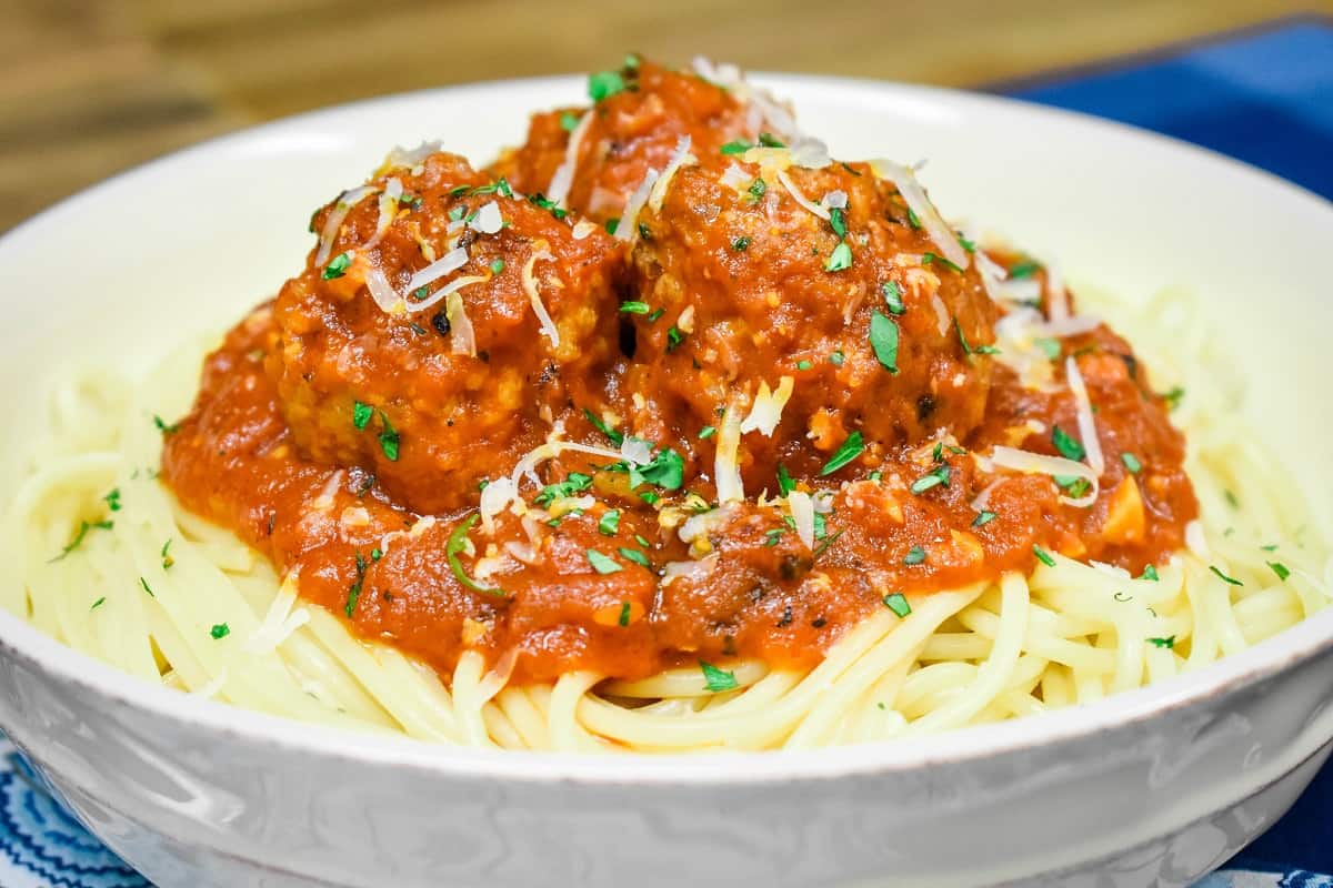 Italian sausage meatballs in a red sauce, served on a bed of spaghetti in a white bowl and garnished with chopped parsley and grated Parmesan cheese.
