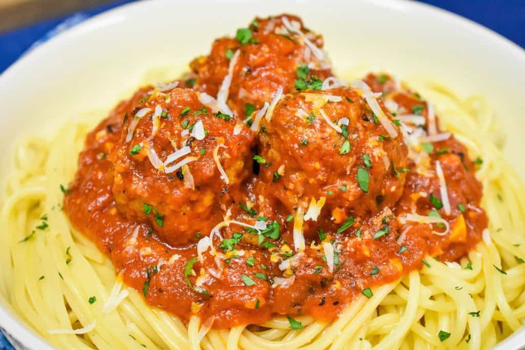 A close up picture of Italian sausage meatballs in a red sauce, on a bed of spaghetti and garnished with chopped parsley and grated Parmesan cheese.